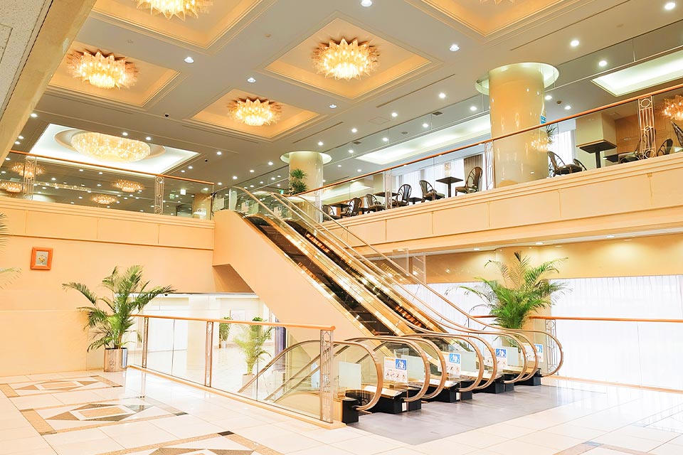 豪華なシャンデリアとエスカレーターを備えた、落合斎場の広々とした受付ロビー